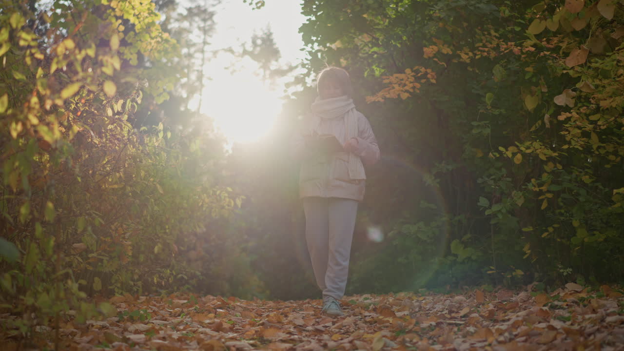 woman walking autumn garden path flipping book pages under warm sunlight glow, golden leaves lining trail, cozy scarf and jacket catching soft light as gentle breeze rustles surrounding foliage