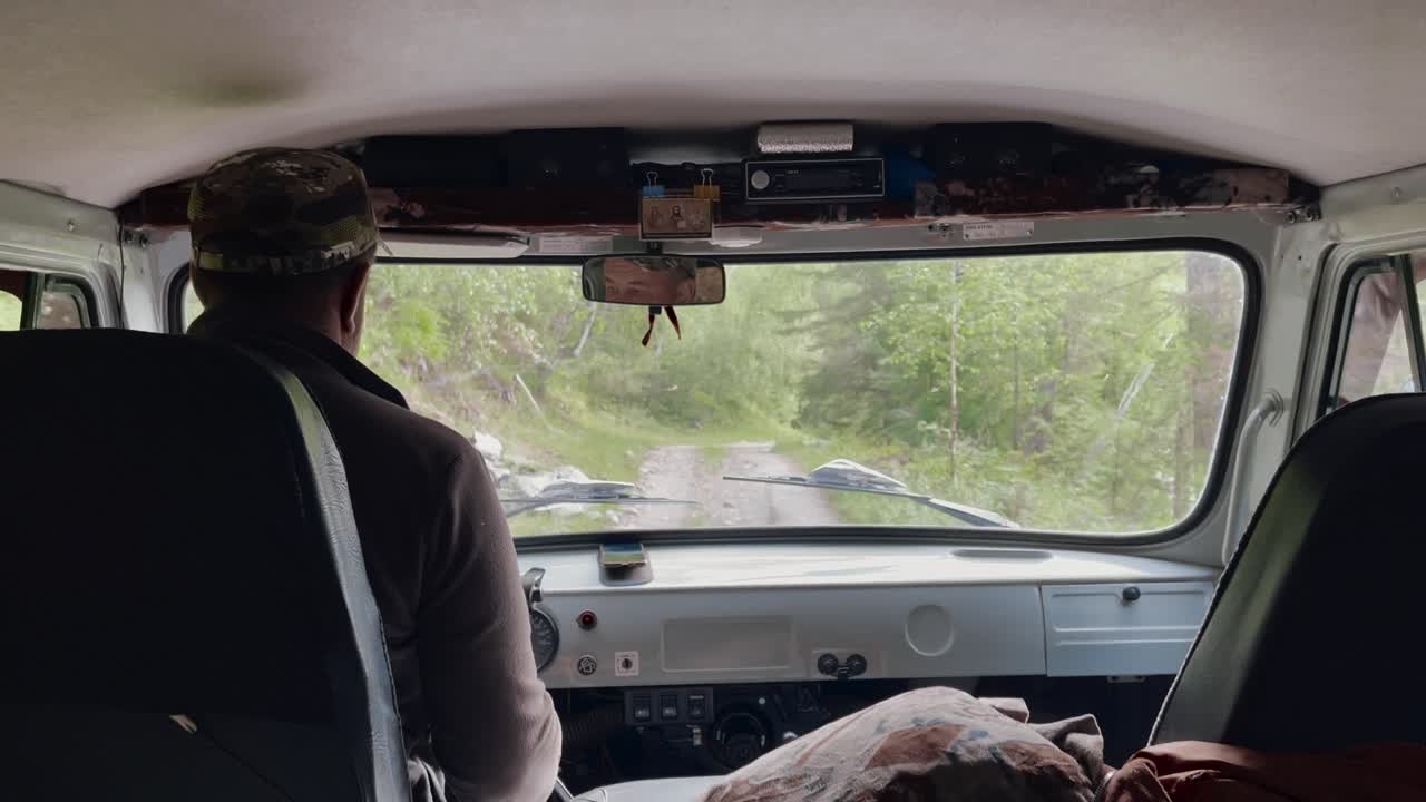 POV dal sedile posteriore all'interno di un veicolo fuoristrada che percorre una pista forestale fangosa nell'Altai, Repubblica dell'Altai, Russia, con un autista e un passeggero durante un viaggio.