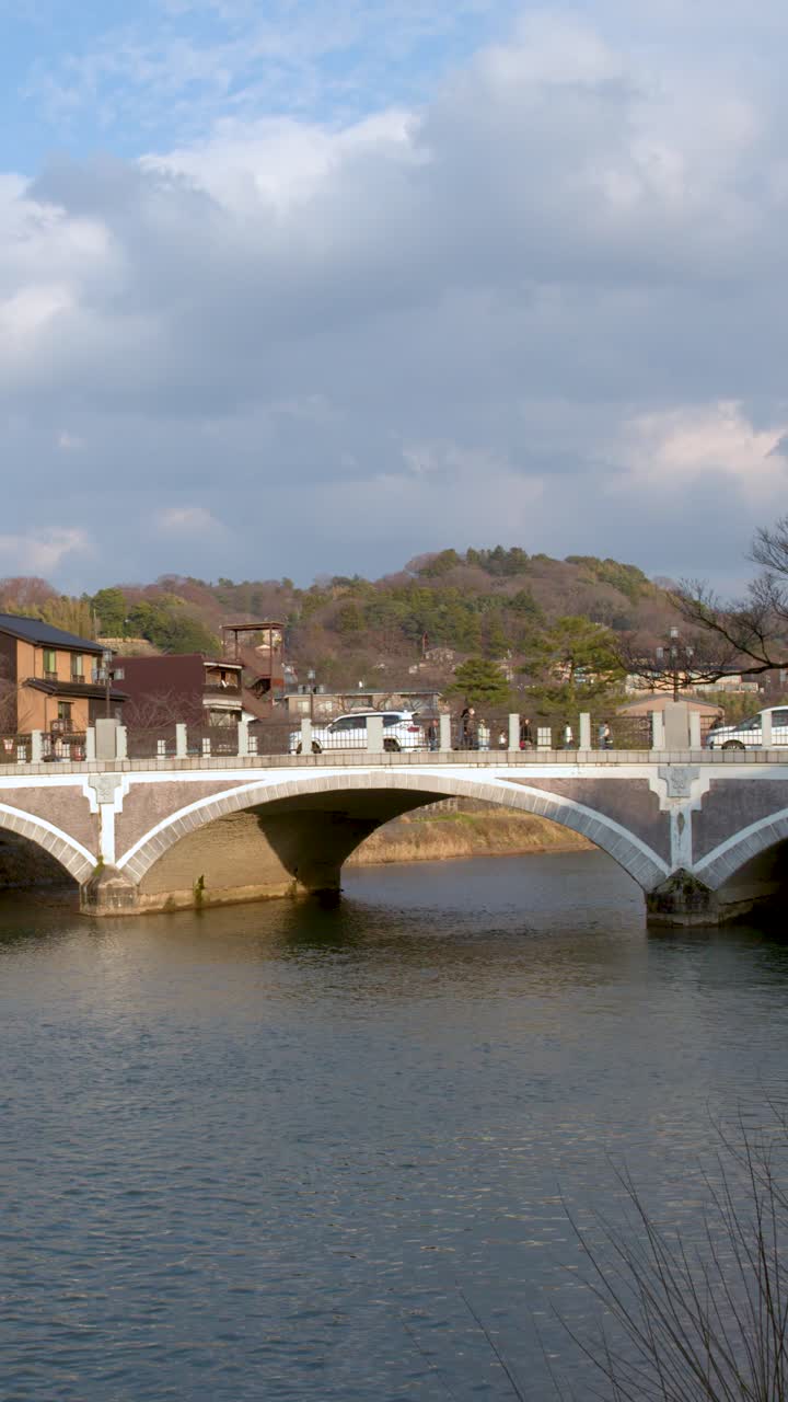 Ampia inquadratura statica di un ponte ad arco in pietra che attraversa un fiume sotto un cielo azzurro nuvoloso.
