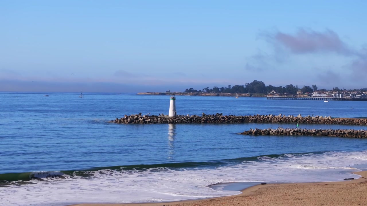 Blacks Beach, molo del faro di Walton, Santa Cruz, California: ripresa aerea con drone di un paesaggio scenografico con barca a vela, onde da surf di un blu intenso, sabbia della marea, Baia di Monterey, Oceano Pacifico. Mattina, cielo blu, nebbia, foschia, movimento circolare a sinistra.