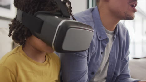 happy biracial man and his son playing video games wearing vr headset