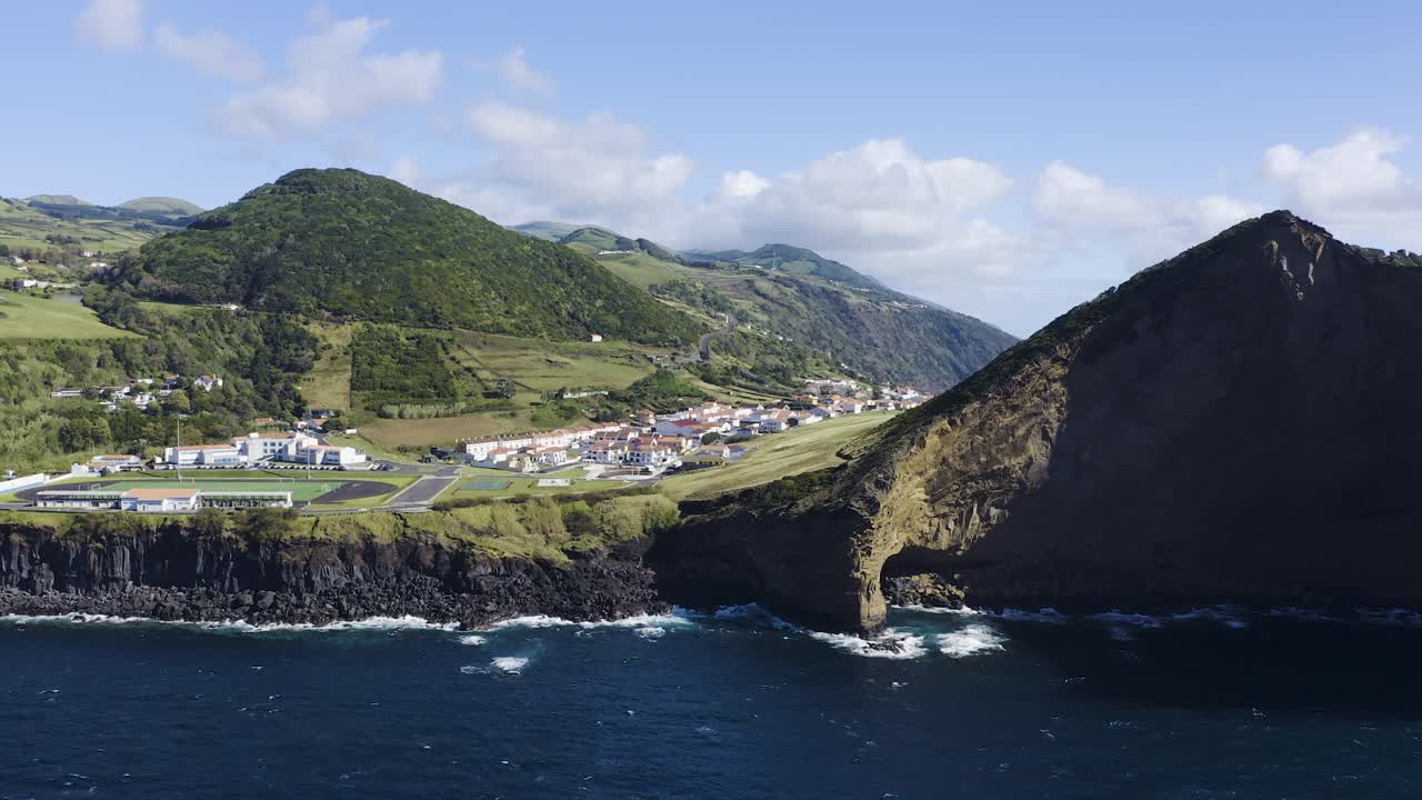 caldera colapsada del volcán que revela un pueblo, un parque de patinaje, un campo deportivo, con montañas, vegetación y formaciones de lava junto al metraje de drones marinos, velas, isla de sao jorge, azores, portugal
