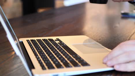 clip taken at coffee shop cafe of a caucasian man typing on computer keyboard then drinking from a coffee cup