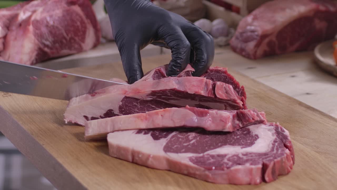 Primo piano di un macellaio che affetta una bistecca di manzo Ribeye cruda e fresca su un tagliere di legno