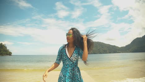 a sexy girl puts her sunglasses on and walks down a jetty with her hair blowing in the wind