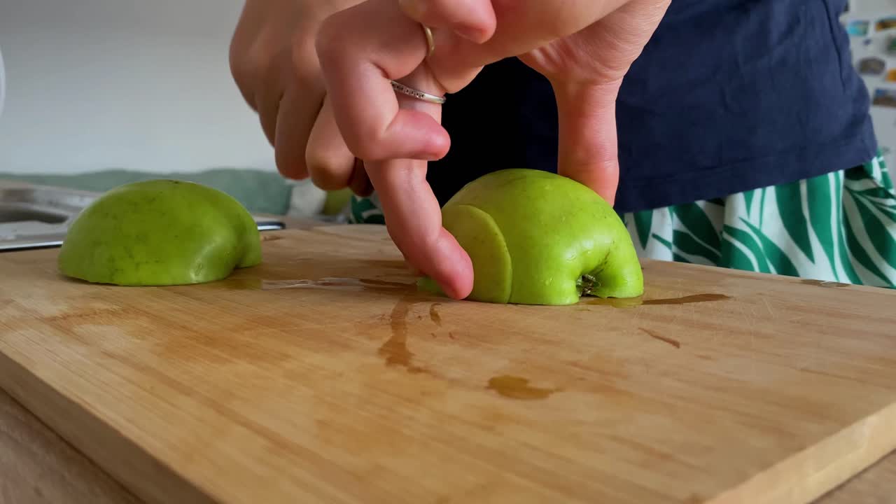 una mujer demuestra sus habilidades culinarias cortando una manzana verde fresca en una tabla de cortar de madera en una cocina bien iluminada, abrazando los valores de una alimentación saludable, desintoxicación y dieta