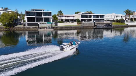 aerial drone footage tracks a speedboat gliding on calm nerang river waters, passing modern waterfront houses under bright daylight with clear blue skies