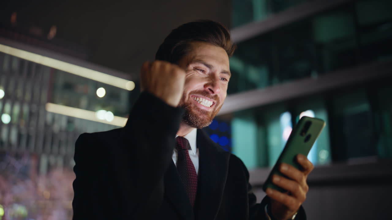 Night businessman reading phone message rejoicing success city lights portrait