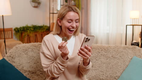 adult woman celebrating bitcoin price surge at home viewing charts on laptop showing victory gesture