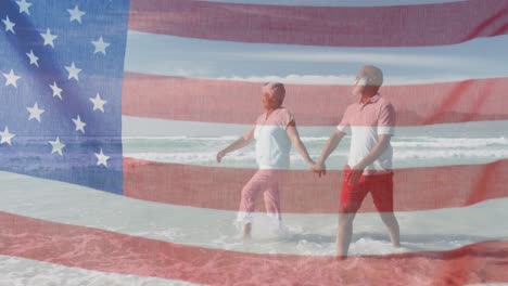 Animación-De-La-Bandera-De-Los-Estados-Unidos-De-América-Sobre-Una-Feliz-Pareja-De-Ancianos-Caminando-Por-La-Playa-Junto-Al-Mar.