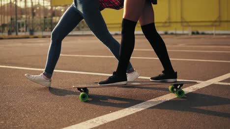 back view of young attractive hipster girl being taught skateboarding by a friend who is supporting her holding her hand