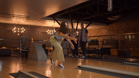 Eine-Junge-Frau-Beim-Bowling-Wirft-Einen-Ball-Auf-Die-Bahn,-Schlägt-In-Zeitlupe-Einen-Ball-Aus-Und-Springt-Und-Tanzt-Vor-Freude.-Eine-Gruppe-Multiethnischer-Freunde-Spielt-Gemeinsam-Bowling.