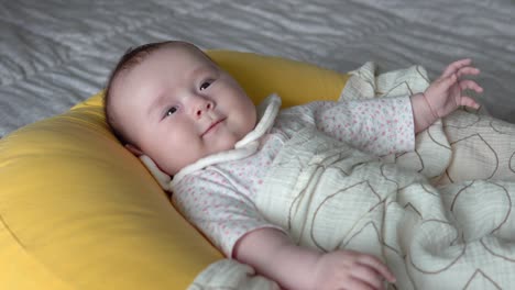 lovable infant baby lying on a cushion on bed smiling - close up