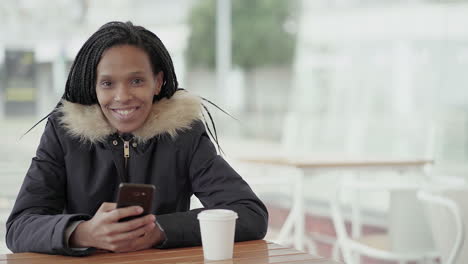 afro-american happy young girl with braids in grey jacket with fur hood sitting outside