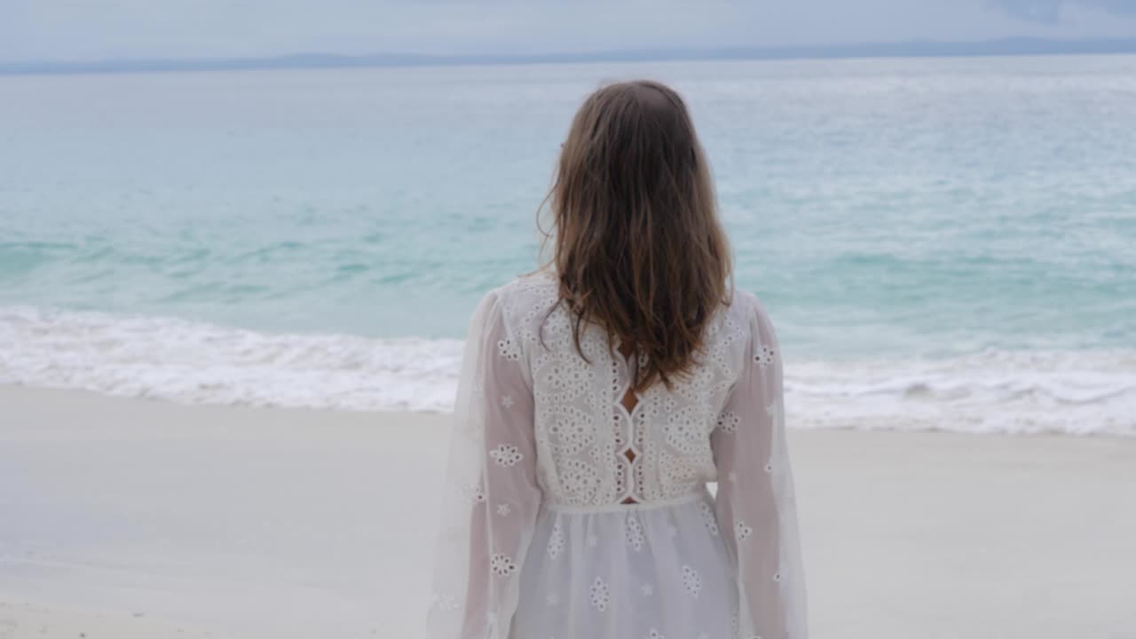인도네시아 북부 수마트라 아수 섬에서 바다를 바라보며 아름다운 해변을 걷고 있는 흰 드레스를 입은 갈색 머리를 가진 여성의 초슬로우 모션 샷