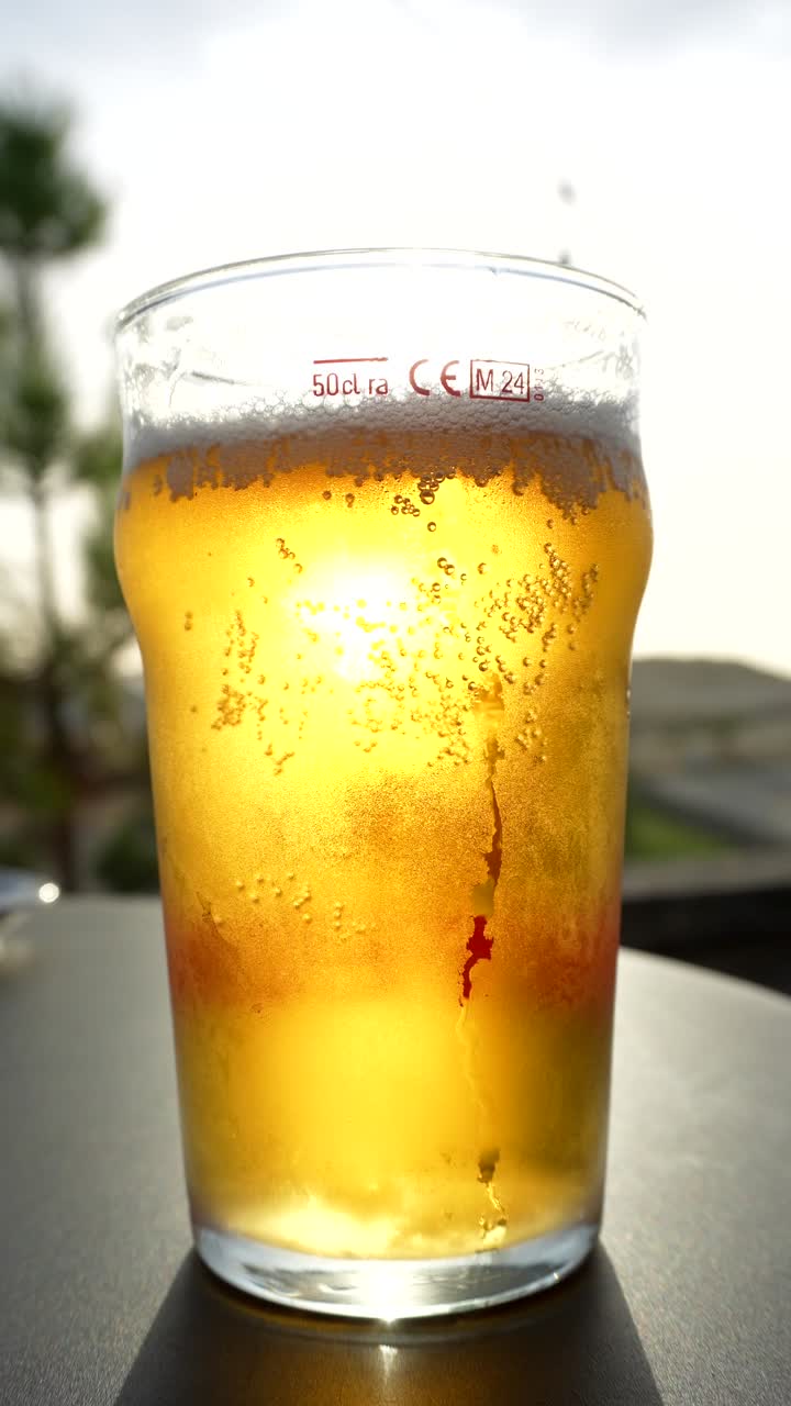 Birra fredda rinfrescante in un bicchiere con bollicine e condensa retroilluminata dalla luce del sole