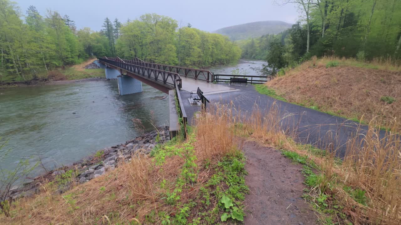 Civilian foot bridge crossing a river in the Appalachian mountains on a foggy, atmospheric day during spring, with benches overlooking the river