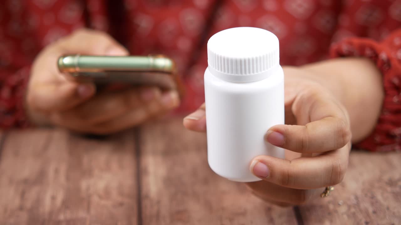 mujer con un frasco de pastillas y usando un teléfono