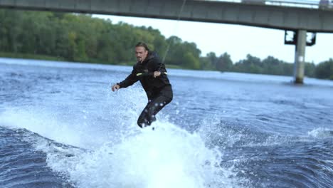 man wakeboarding on river waves under city bridge in slow motion