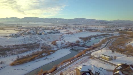 aerial view of a neighborhood with children sledding down a slope near a river and bridge with mountains and a sunset in the background