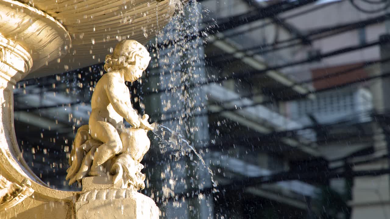 La luce del sole illumina una statua di cherubino in pietra mentre l'acqua schizza dalla storica Fontana Carriedo