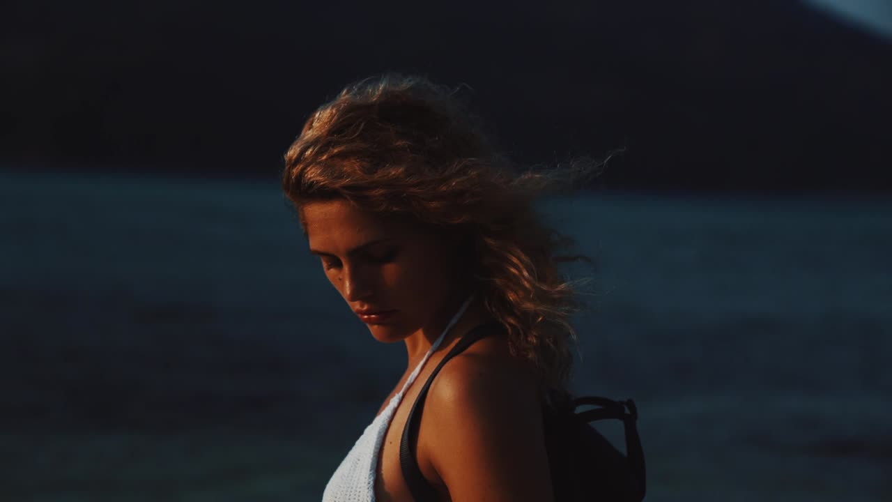 A young brunette woman is enjoying herself at a tropical beach by sunset. The sun is creating a golden light and her hair is moving in the wind on the Perhentian Islands in Malaysia in slow motion.