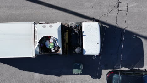 static top down aerial drone footage where a dump truck drives into view and picks up a trash can to dump.