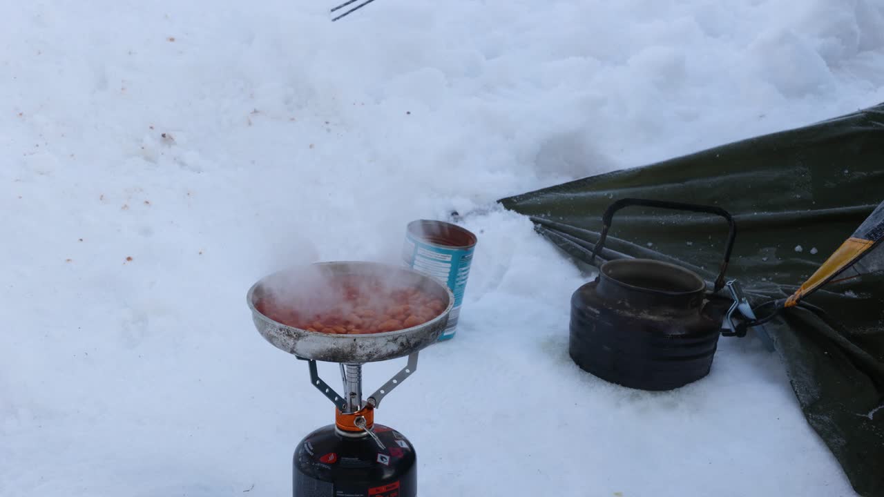 frijoles horneados cocinados y revueltos en una cocina de gas en la nieve mientras acampan