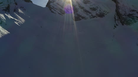 panorámica para revelar la cresta de la montaña cubierta de nieve con el sol detrás con la llamarada del sol, en los alpes franceses en invierno