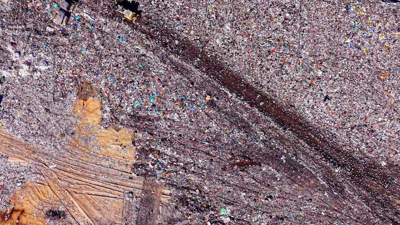 Vista aérea de diversos resíduos domésticos sendo processados por máquinas pesadas. Padrão abstrato de materiais de descarte em aterro sanitário com pássaros voando sobre o lixo.