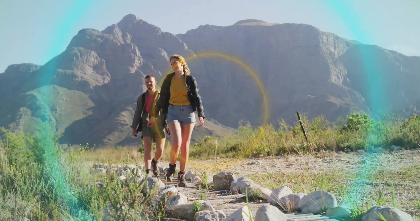 Donna che sale su assi di legno, attivando anelli tecnologici intorno a escursionisti che camminano su un sentiero di montagna