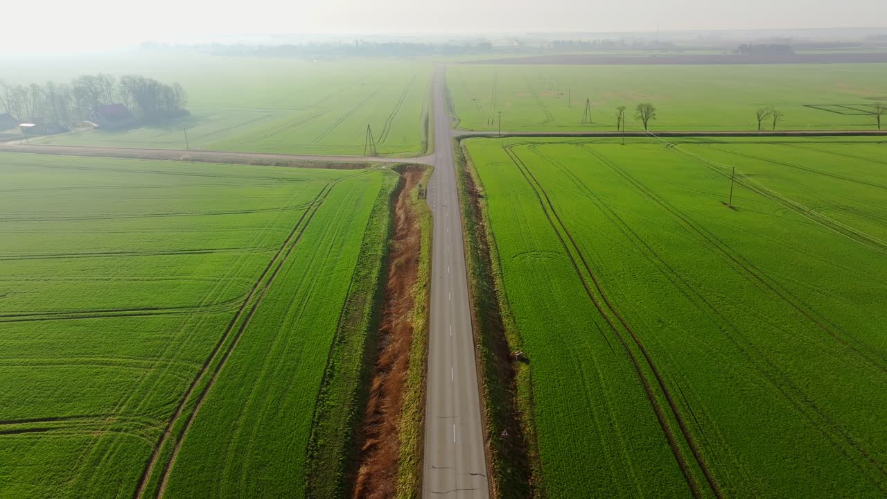 Drone glides in straight motion above rural highway with morning mist, soft sun