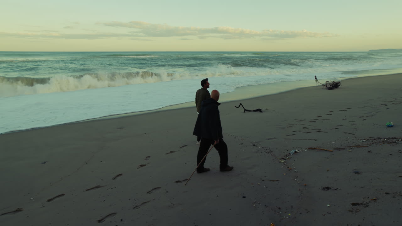 Two Men Watch the Stormy Ocean Waves Crash on the Beach in the Morning