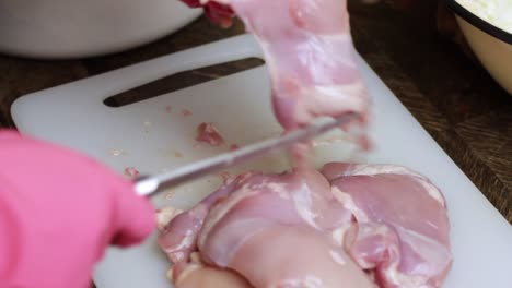 persona con guantes de goma cortando pechuga de pollo cruda con un cuchillo afilado