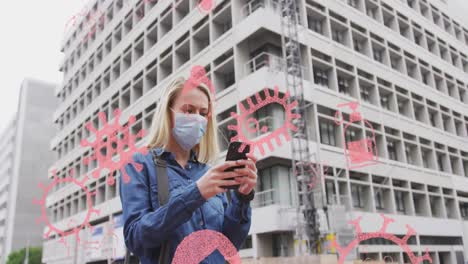animation of virus cells and icons over caucasian woman wearing face mask