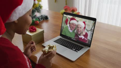 African-american-woman-with-santa-hat-using-laptop-for-christmas-video-call-with-couple-on-screen