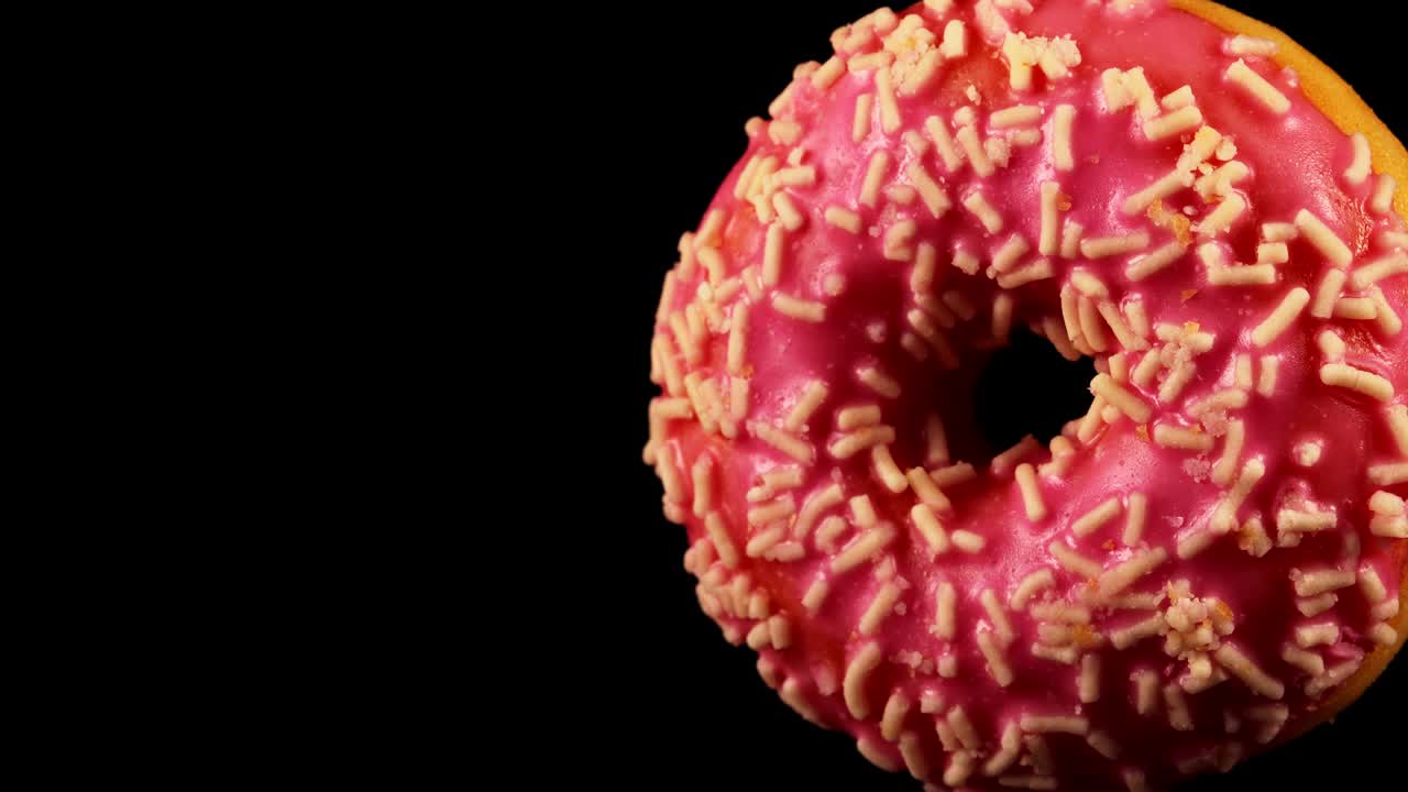 donut de vidrio rosado con salpicaduras sobre un fondo negro.