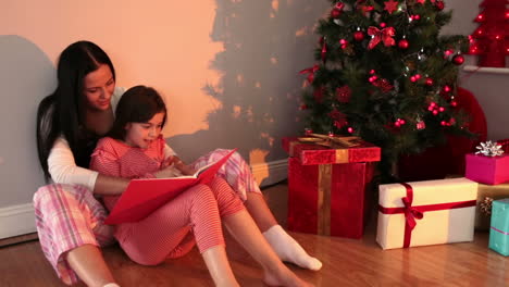 mother reading her daughter a story by the christmas tree