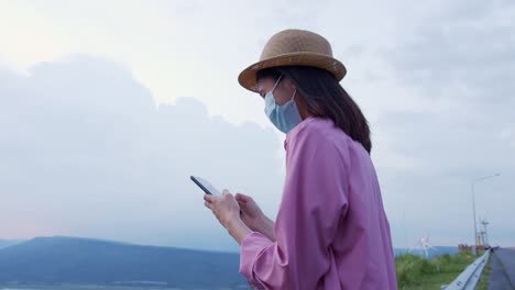 tiro de mano: mujer turista sosteniendo un teléfono de pantalla verde por la noche y una mujer usando una máscara para prevenir enfermedades.