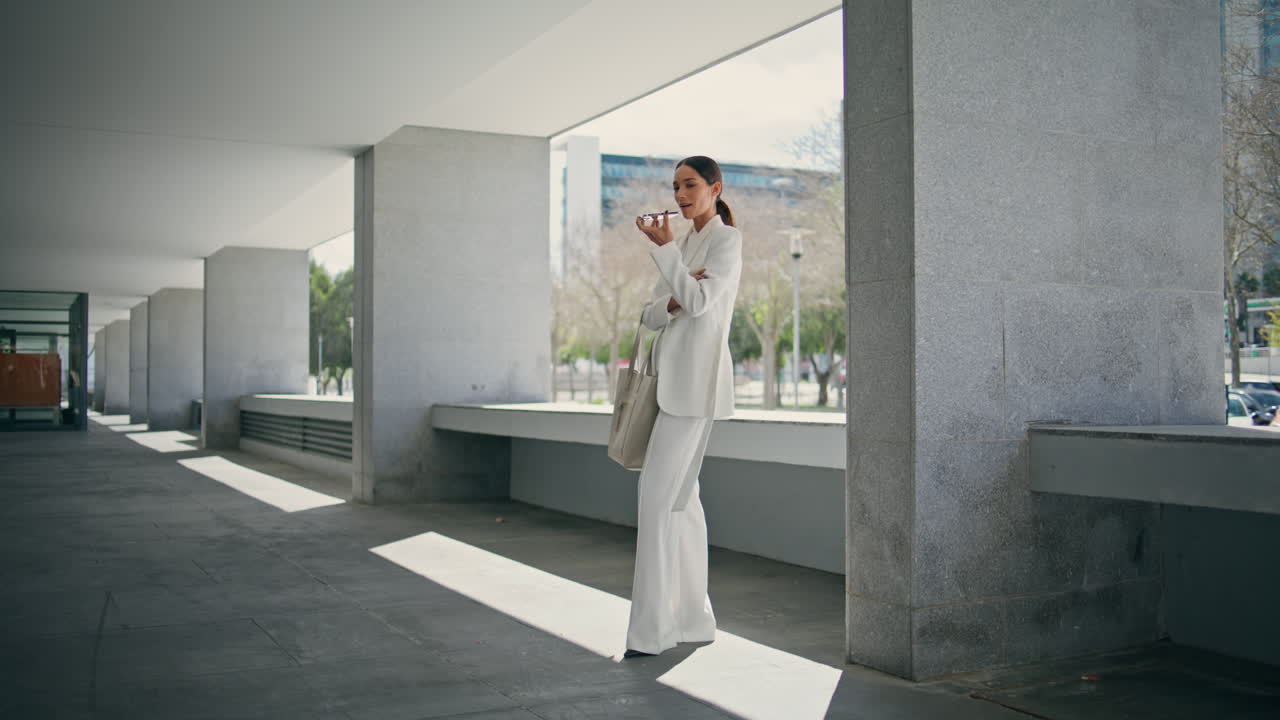 mujer de negocios grabando un mensaje de voz de pie en el estacionamiento de la oficina en un día soleado.