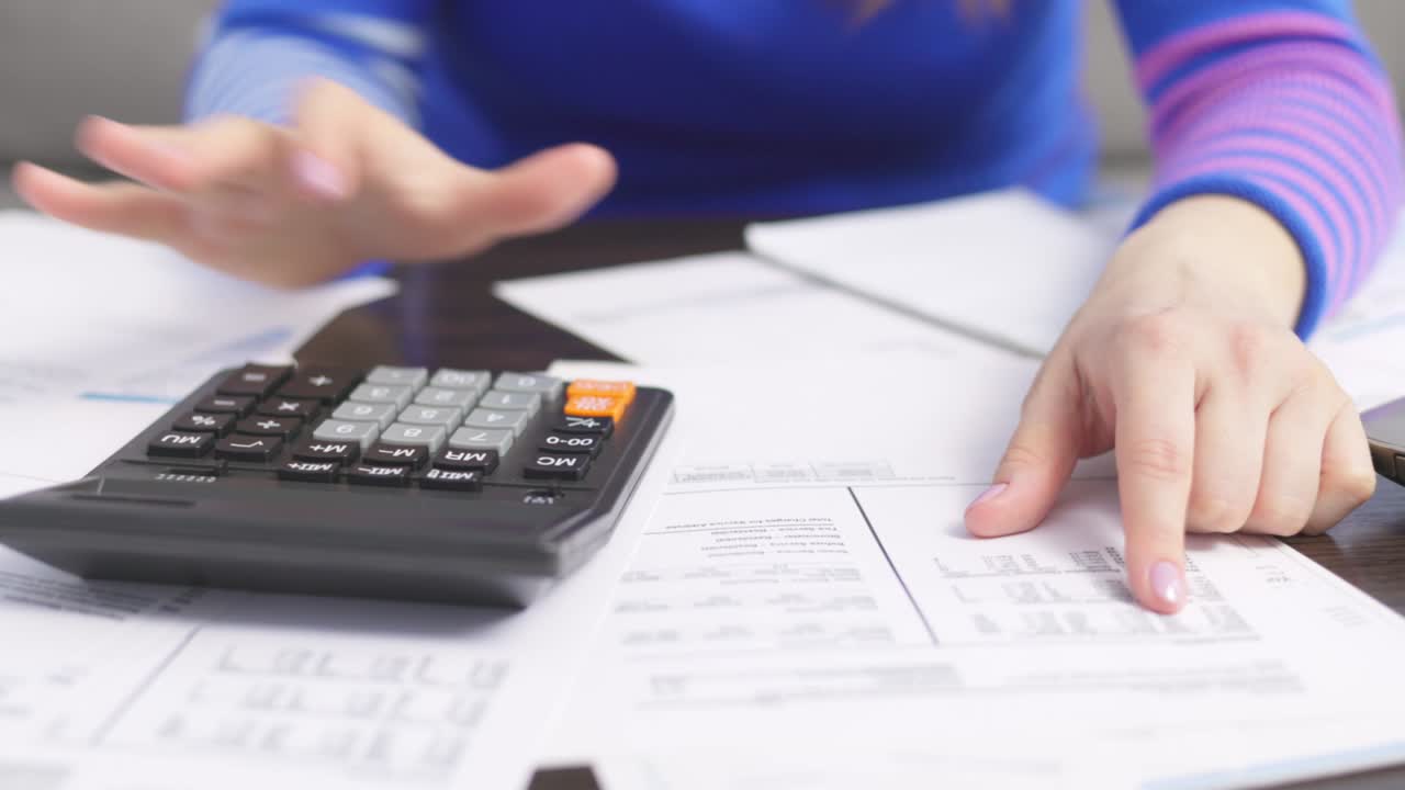mujer usando calculadora para calcular facturas domésticas en el hogar, haciendo papeleo para pagar impuestos