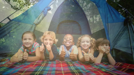 children giving thumbs up over camping tent and forest background