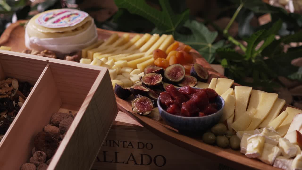 Wooden board with assorted cheeses, figs, olives, dried fruits, and jam in a rustic setting