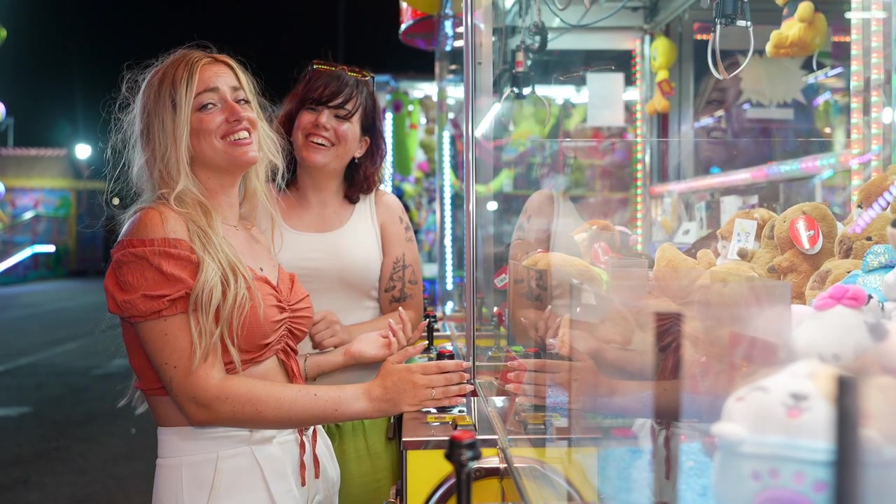 Due giovani donne che giocano alla macchina artiglio a un luna park notturno