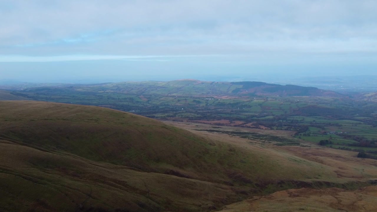 Ampia veduta aerea paesaggistica delle colline del Parco Nazionale Brecon Beacons Bannau Brycheiniog con uno sfondo di campagna rurale e cielo nuvoloso in 4K.