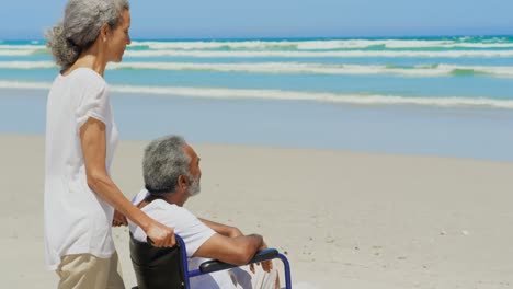 Vista-Lateral-De-Una-Mujer-Afroamericana-Senior-Activa-Con-Un-Hombre-Senior-Discapacitado-En-La-Playa-Bajo-El-Sol-4k