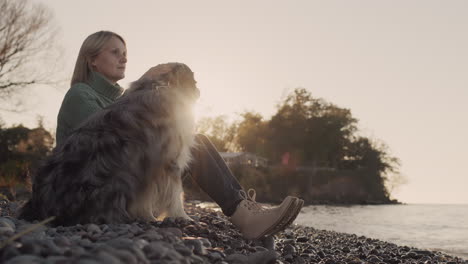 a woman with her dog is resting on the shore of a lake on a clear autumn day