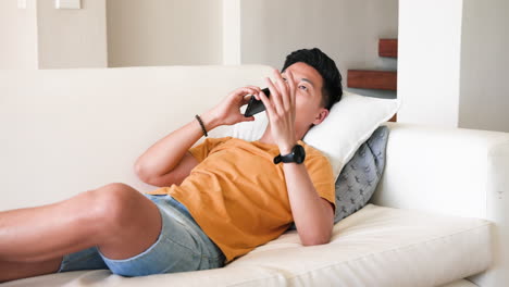 relaxing at home, young man talking on smartphone while lying on couch