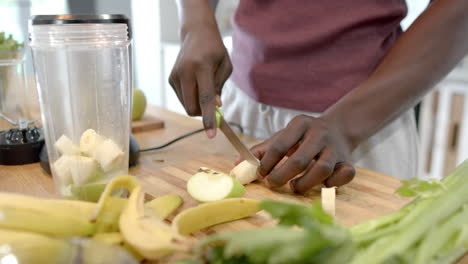 Sección-Media-De-Un-Hombre-Afroamericano-Preparando-Batidos-Saludables-En-La-Cocina-De-Casa,-Cámara-Lenta