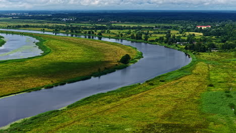 picturesque drone shot of river passing through green fields over a vast green landscape during daytime